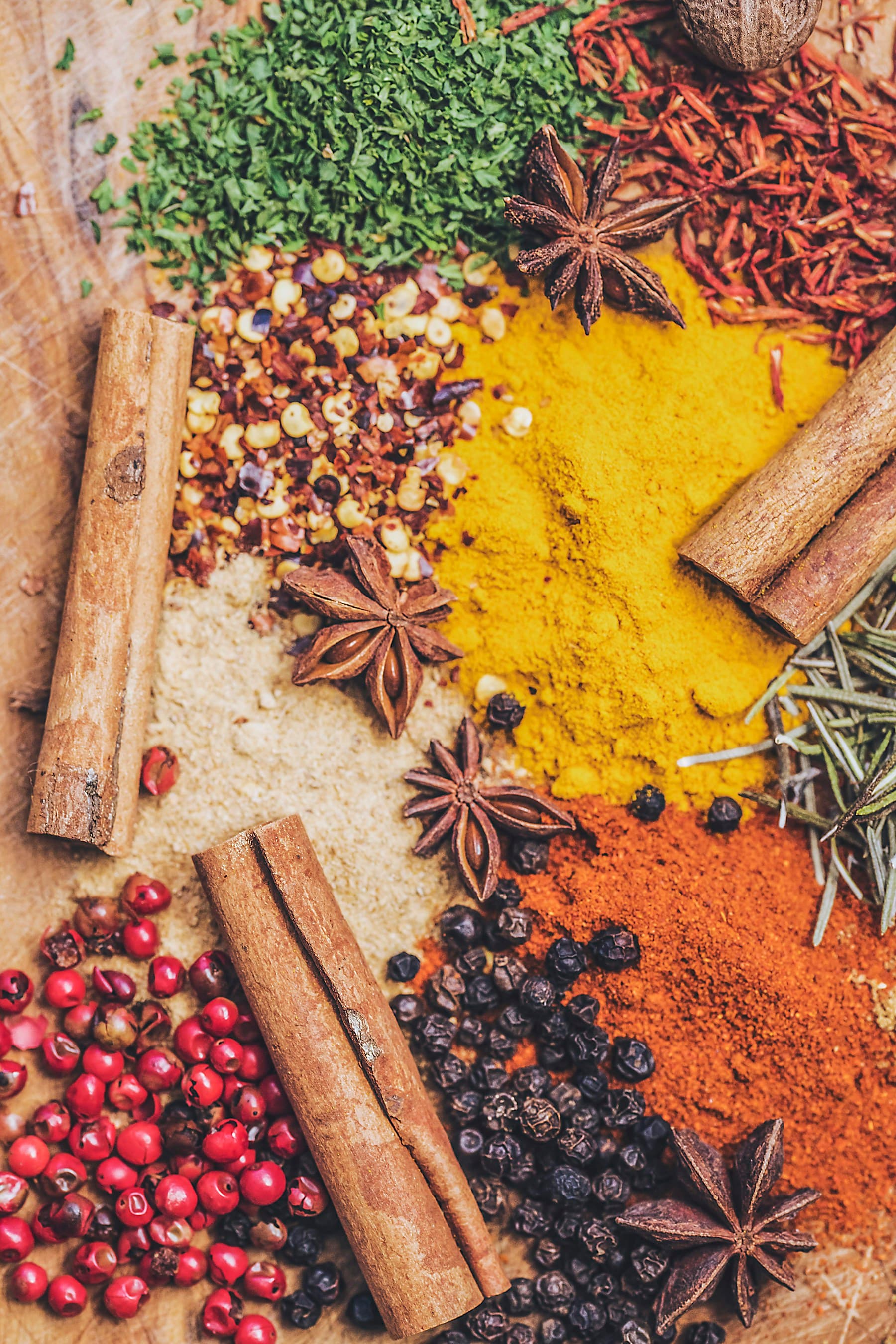 Cinnamon, star anise, peppercorns, herbs, and colorful ground spices on a wooden surface